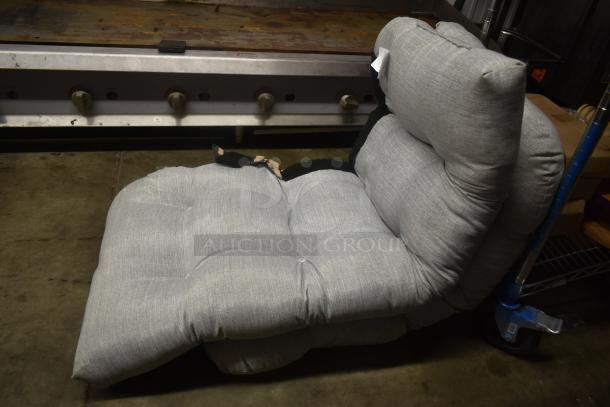 Gray tufted floor chair with a cushioned backrest, slight wear and tear visible, positioned on a concrete floor.