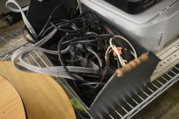 Box of assorted power cables and cords in used condition, with visible tags and plug ends.