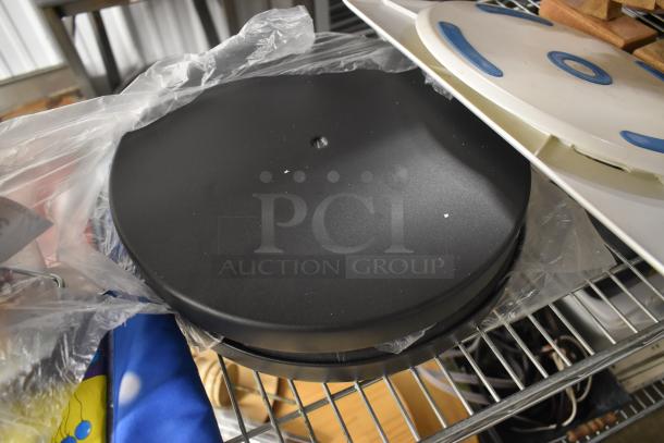 Black round turntable platter, plastic wrapped, on metal shelf, good condition. Ideal for vinyl records, no visible markings.