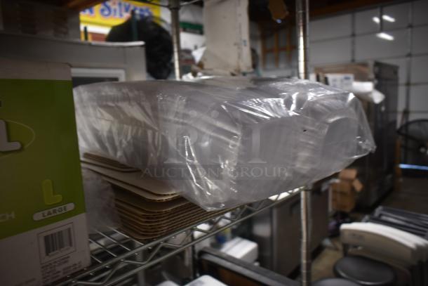 Stack of plastic food containers wrapped in plastic on a metal shelf, next to cardboard inserts and a "Large" size packaging box.