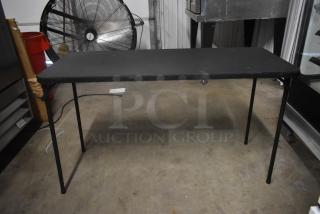 Black folding table with metal legs, showing signs of wear. Ideal for temporary setups or garage sales.