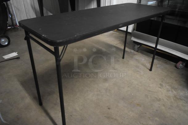 Black folding table, rectangular, metal legs, minor surface wear, suitable for meetings or events. Durable and functional.