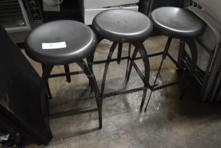 Three black metal bar stools with smooth seats and sturdy frames. One stool has a visible auction tag marked "38." Good condition.
