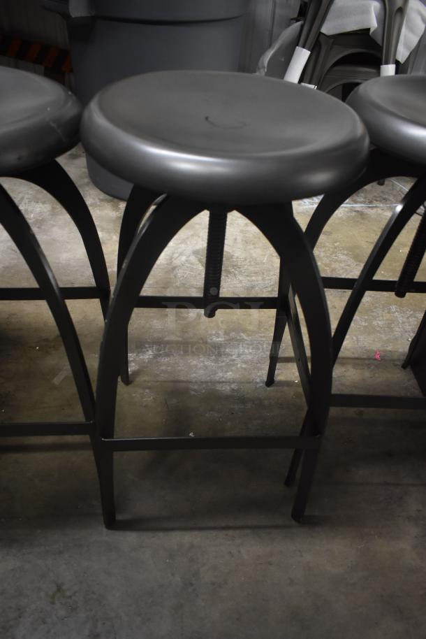 Black metal bar stools with rounded seats, adjustable height mechanism, and sturdy legs. Good condition.