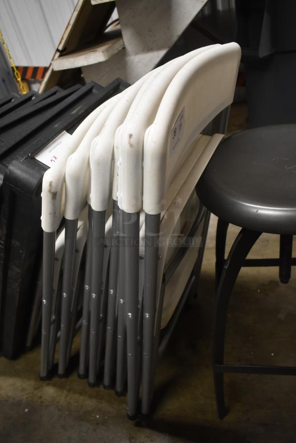 Set of white folding chairs with gray metal legs, in fair condition. Auction tags visible, indicating lot number.