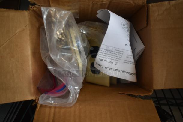 Open cardboard box containing various small items in plastic bags and instruction manual. Condition and details unknown.
