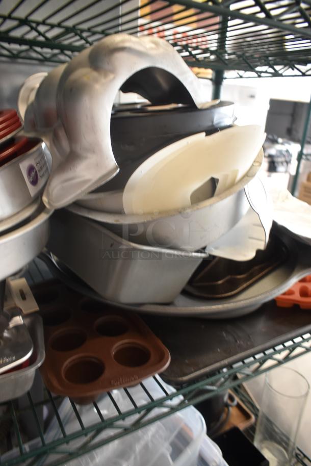 Assorted bakeware stack, including muffin and cake pans and a bundt mold. Visible brand label: Wilton. Used condition.