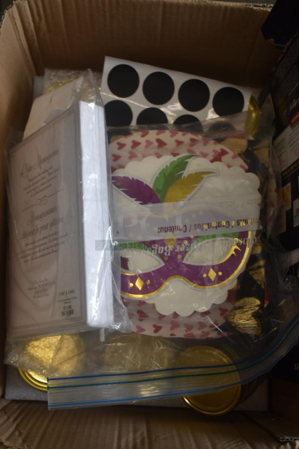 Box of assorted party supplies including masks, monogram cake toppers, and decorative materials. Items in new condition.