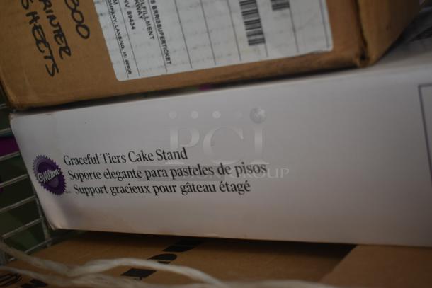 Wilton Graceful Tiers Cake Stand in box, labeled in English, Spanish, and French. Box shows slight wear.