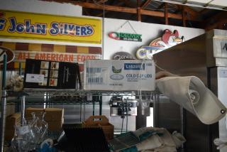 Assorted restaurant supplies including glass pitchers, cold cup lids, and rolled fabric on metal shelving.