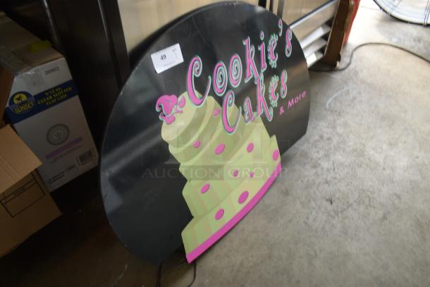 Vintage "Cookie's Cakes & More" metal sign featuring vivid colors and cake graphic, minor wear, auction lot 49.