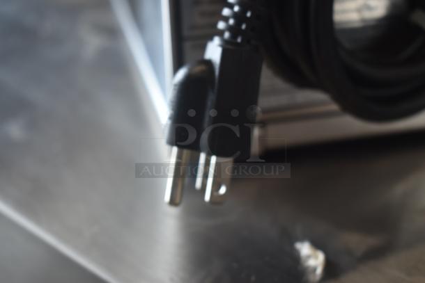 Close-up of a black electrical plug with two prongs, attached to a cord. Plug appears in good condition.