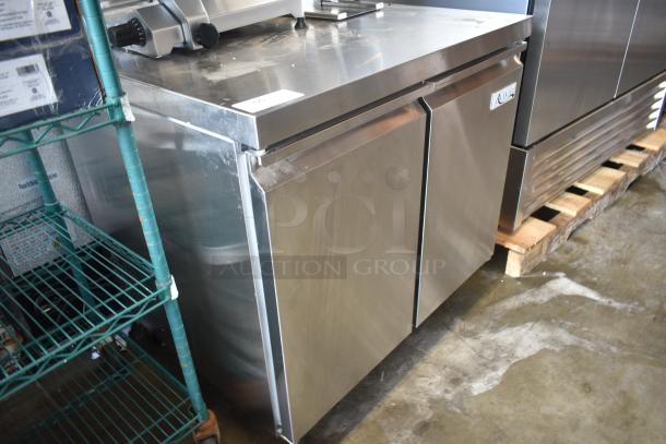 Stainless steel commercial refrigerator with double doors, branded "True." Slight surface wear visible.