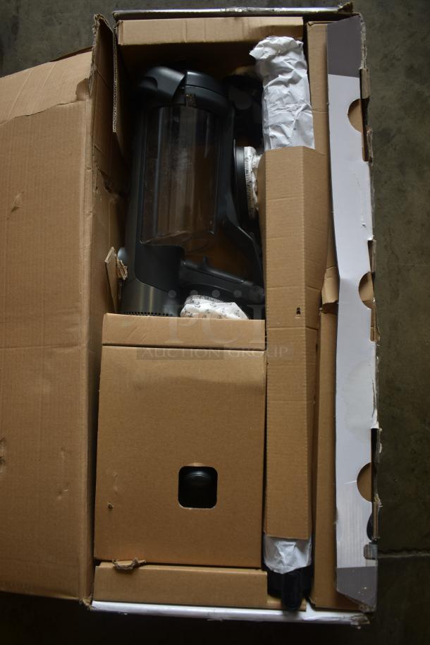 Vacuum cleaner in original packaging, partially unpacked; black and clear components visible. Box shows slight wear.
