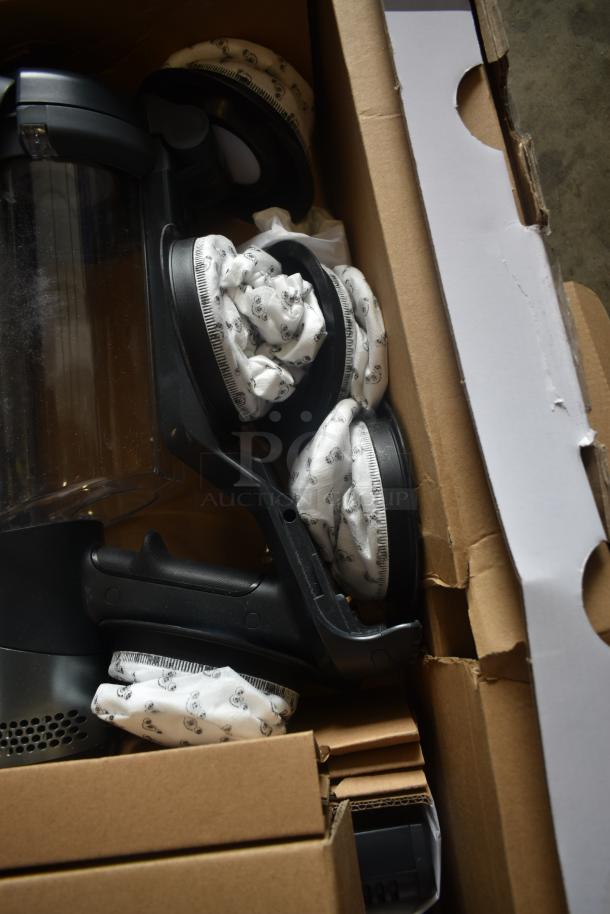 Vacuum cleaner packaged in a cardboard box, featuring black handles and clear canister, wrapped in protective material.