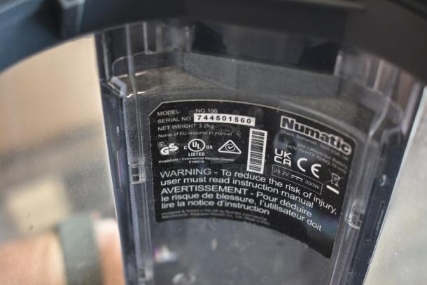 Numatic vacuum cleaner label showing model no. 100, serial no. 744501560, net weight 3.2 kg, safety warnings, and compliance logos.