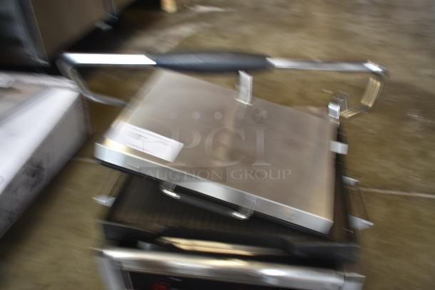 Stainless steel panini press with visible handle, label indicating model or lot number. Slightly blurry condition.