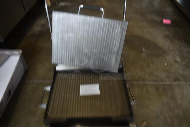 Commercial panini press with ribbed plates, metal handle, slight wear, visible label with usage instructions.