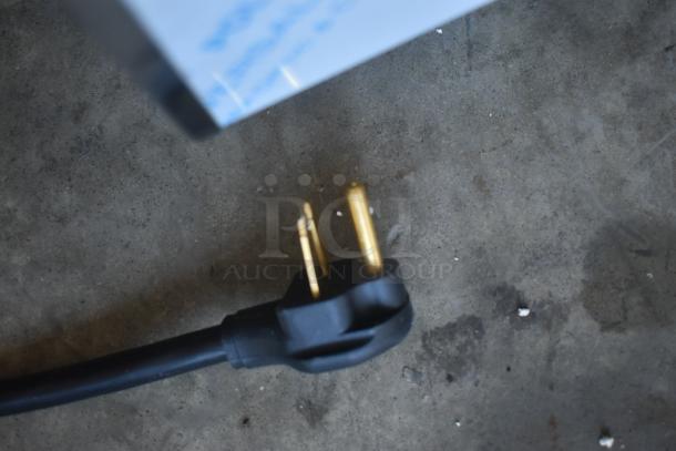 Black electrical plug with three gold prongs on a concrete surface, in good condition.