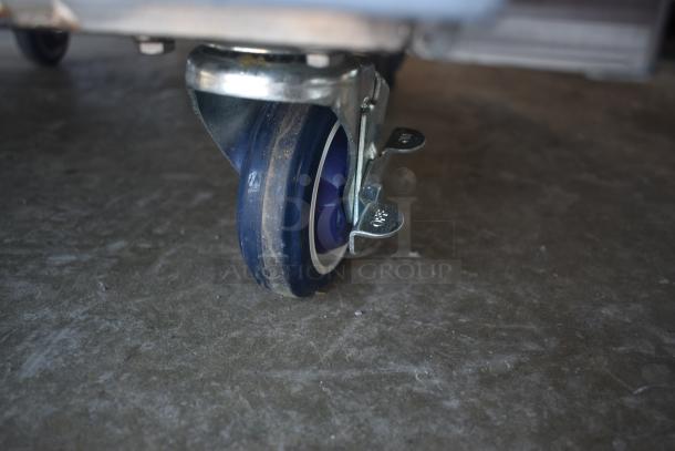 Blue caster wheel with metal bracket and dual brake levers marked "ON" and "OFF," on a concrete surface. Moderate wear.