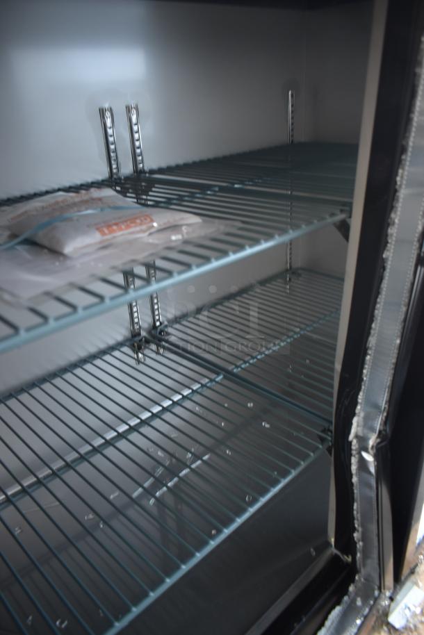 Empty commercial refrigerator interior with adjustable wire shelves, clean condition. A packet is placed on one shelf.