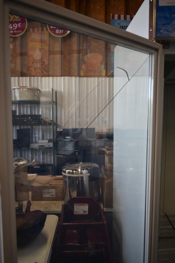 Storage room with various electronic equipment and a stainless steel appliance. Items are on metal shelving; lighting is dim.