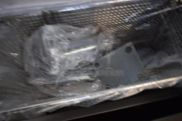 Blurry image of metal parts wrapped in plastic, placed inside a metal mesh basket. Condition and specifics unclear.