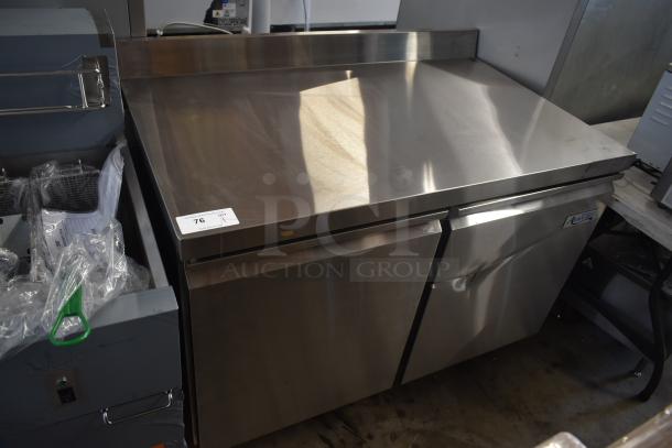 Stainless steel commercial refrigerator with dual doors, durable surface, and light scuffs. Tag marked "76."