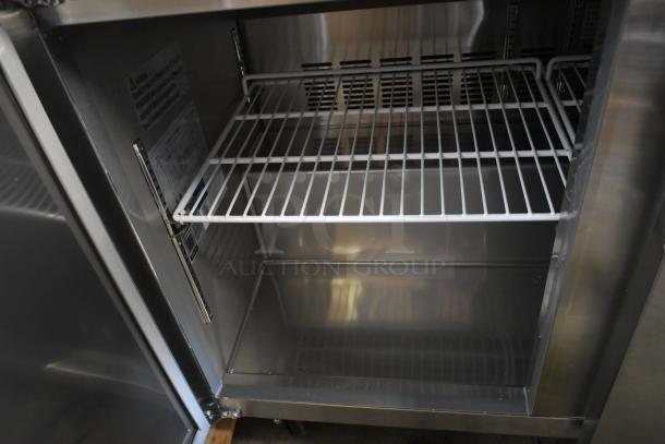 Commercial-grade stainless steel refrigerator, interior view showing clean wire shelves and ventilation. Visible safety label inside.