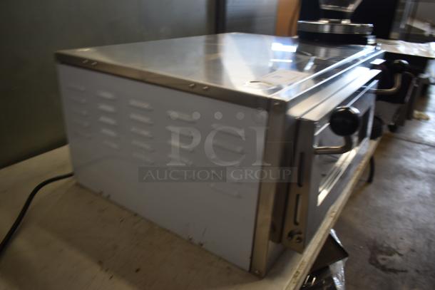 Stainless steel countertop pizza oven, side view, vented design, black handle, power cord attached, in good condition.