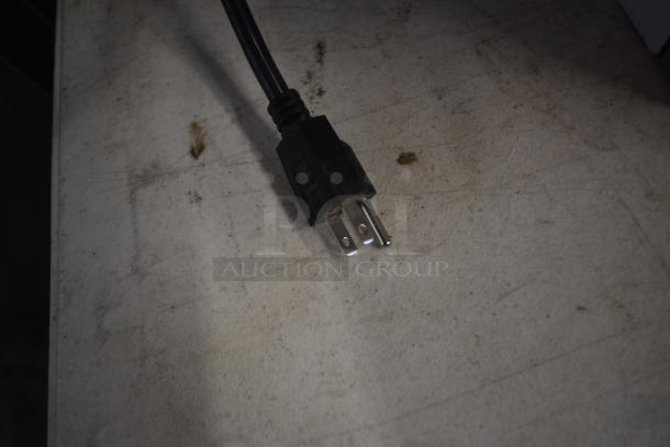 Electrical three-prong power plug on dusty surface, in used condition. Black casing with visible wear, suitable for standard outlets.