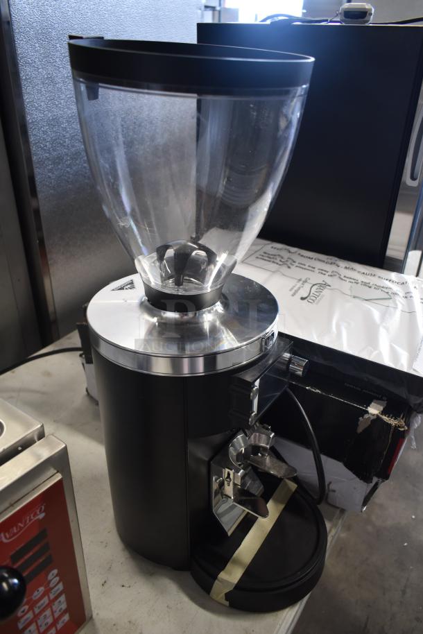 Commercial coffee grinder with transparent bean hopper, shiny metallic top, and black base. Appears in good condition.