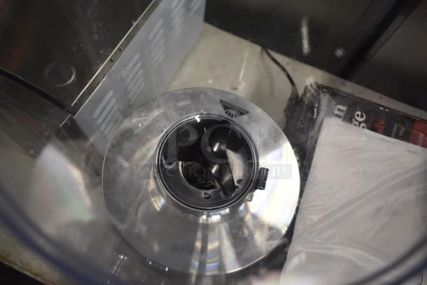 Close-up of a metal mixing blade inside a transparent container, showing slight wear. Marking reads "WARNING."