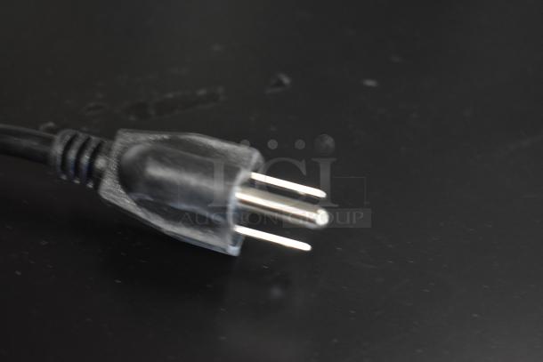 Close-up of a black three-prong power plug with a sturdy design, shown on a dark background, in excellent condition.