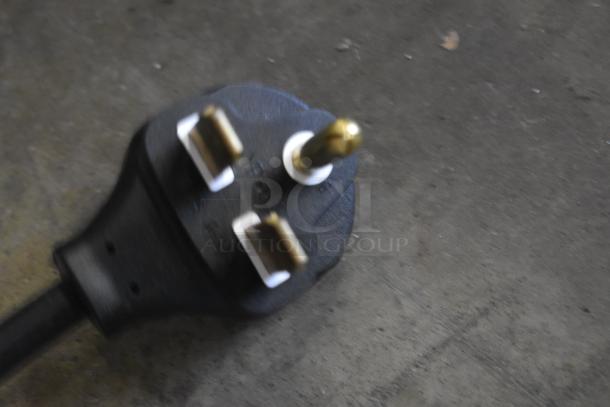 Close-up of a black power plug with three brass pins, slightly blurred. Suitable for auction, condition appears used.
