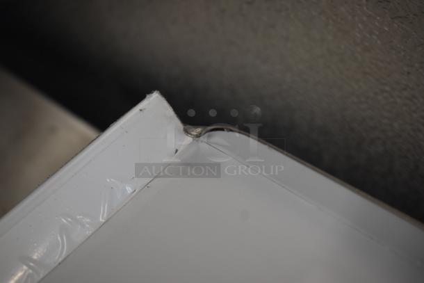 Close-up of a dented white metal sheet corner, showing minor wear and a curled edge.