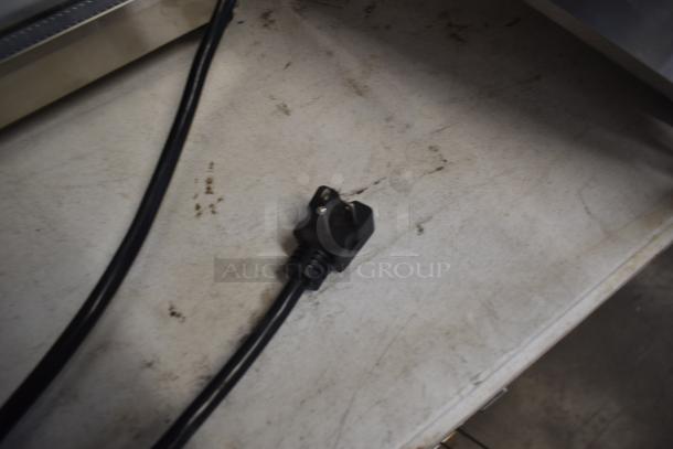 Black power cord with a three-prong plug on a dusty, scratched surface.