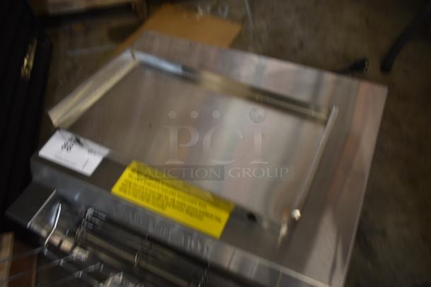 Blurry image of a metal appliance with a handle, possibly a grill or oven component. Labels and markings are unreadable.