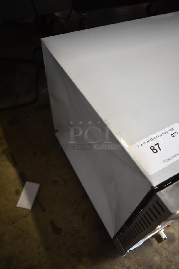 White metal appliance with scratches, auction tag number 87, visible controls on one side, some wear marks.