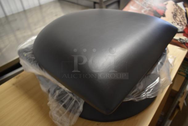 Black leather motorcycle seat, unused, wrapped in protective plastic, pristine condition, no visible tags or markings.