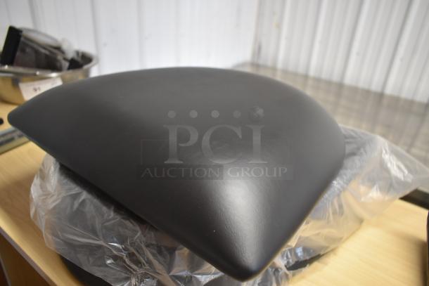Black leather motorcycle seat, in excellent condition, with a sleek, contoured design on a plastic-covered wooden table.