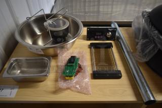 Assorted kitchen equipment including stainless steel bowls, slicer, digital display unit, and metal tube on wooden surface.
