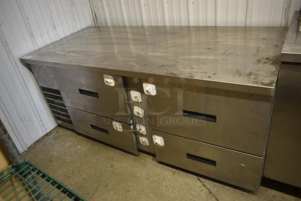 Commercial stainless steel refrigerated prep table with four drawers, visible wear, sturdy construction, ideal for kitchen use.