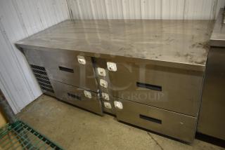 Commercial stainless steel refrigerated prep table with four drawers, visible wear, sturdy construction, ideal for kitchen use.