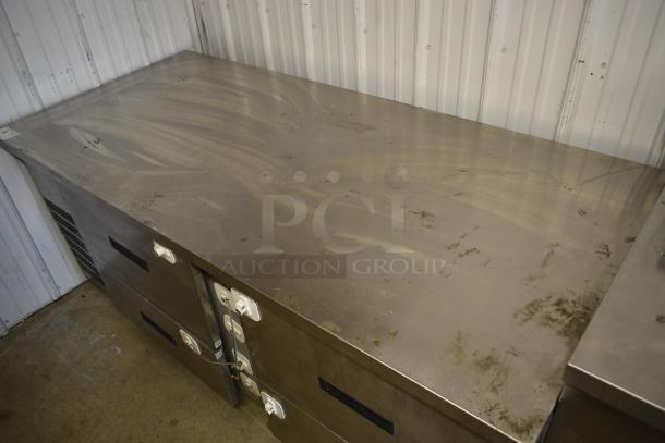 Stainless steel commercial kitchen counter with storage drawers, visible wear and scratches, secure locks on handles.