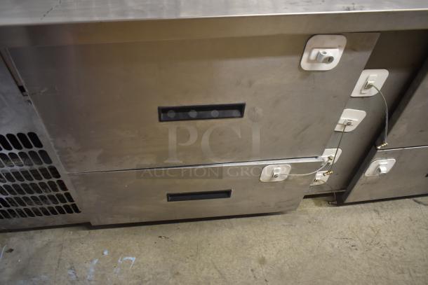 Stainless steel commercial undercounter freezer with locking mechanism, two black handles, and visible wear marks.