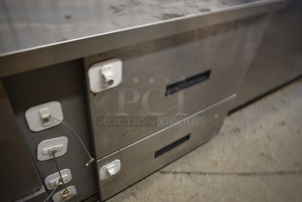 Stainless steel commercial refrigerator with double drawers, security tags, and cable seals, showing signs of wear.