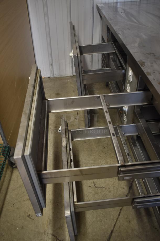 Stainless steel workbench with multiple open drawers, minor surface wear, ideal for heavy-duty storage and workspace needs.