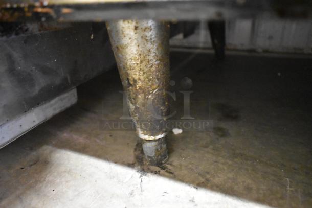 Rusty metal table leg, worn condition, attached to a metal surface. No visible labels or markings.