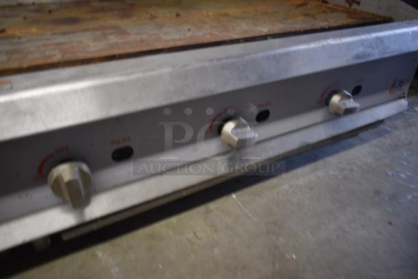 Commercial metal griddle with three control knobs. Worn surface indicates use. Controls labeled "OFF" and "PILOT".